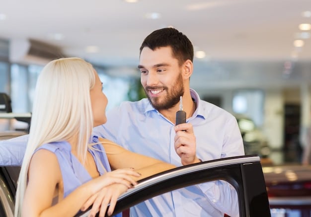 A young couple happily receiving the keys for their new car from a dealership representative. The dealership is modern and clean, with other cars visible in the background.