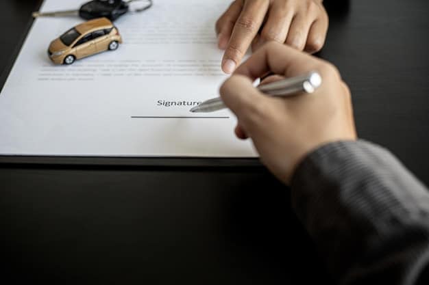 Close-up of a person's hand signing a car loan agreement with a pen on a wooden desk, highlighting the importance of careful review of terms and conditions. A calculator and a set of keys are scattered near the document.