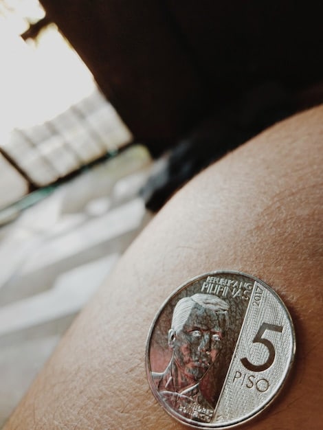 A close-up shot of a hand holding a Mexican peso coin, with a blurred background showing an office environment, symbolizing financial security and the AFORE system in Mexico.