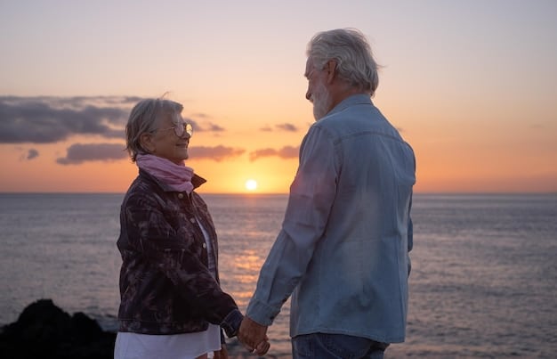 A senior couple smiling and holding hands while overlooking a peaceful beach at sunset, symbolizing a happy and secure retirement.
