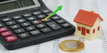 Calculadora mostrando números ascendentes junto a una casa miniatura y moneda mexicana, representando el impacto de la inflación en pagos hipotecarios.