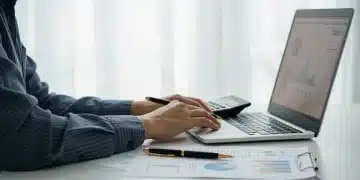 Persona calculando su capacidad de endeudamiento automotriz en una laptop, con documentos financieros.